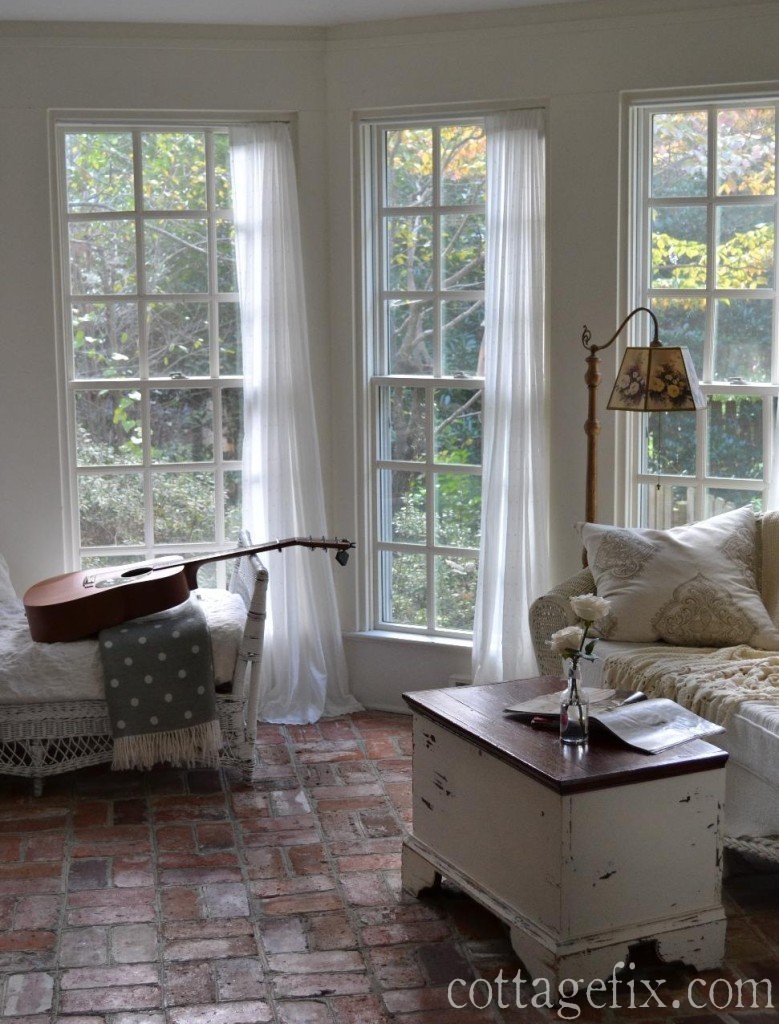 Cottage Fix blog - sun porch with white sheer curtains, brick floors, wicker, and a chippy paint trunk